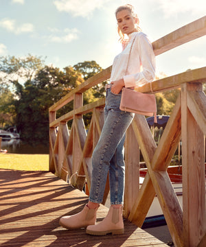 women wearing the suummer boudica performance ankle bootsin blush nubuck, holding the finsbury clutch beg and the sennowe belt in blush suede, a very light pink hue- perfect for summer.